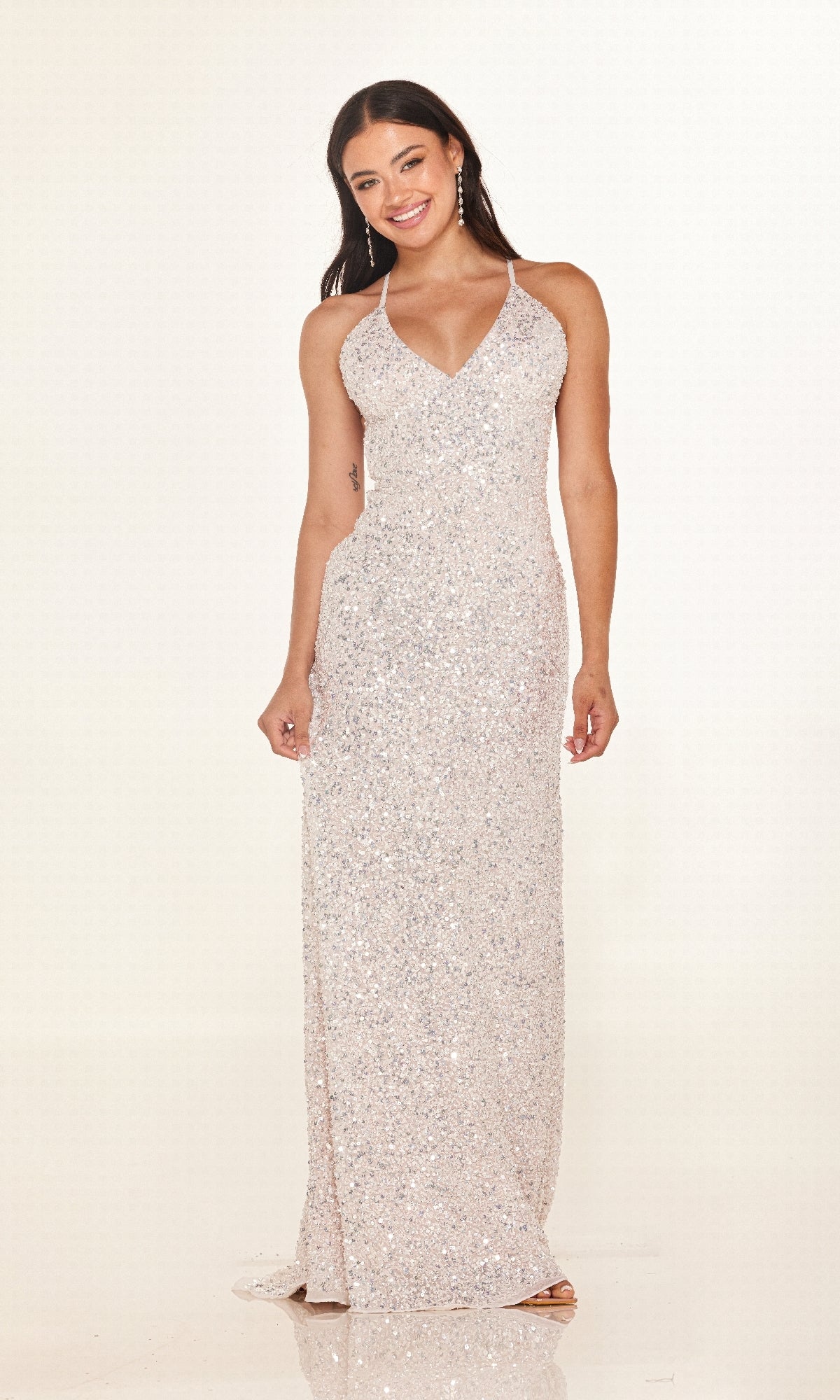 A woman stands and smiles against a plain light background, wearing the Cecilia Couture 2640 long prom dress—a sleeveless, floor-length silver sequin gown with a V-neckline.